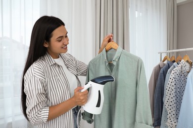 Woman steaming shirt on hanger at home