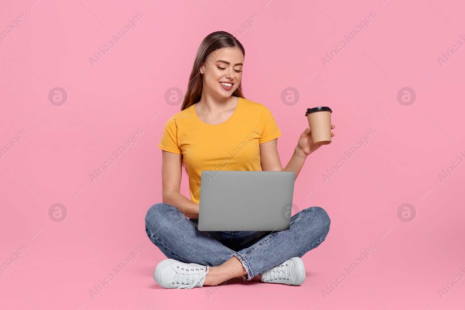 Photo of Happy woman with laptop and paper cup on pink background