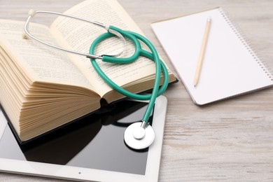 Book, tablet, stethoscope and notebook on wooden table. Medical education