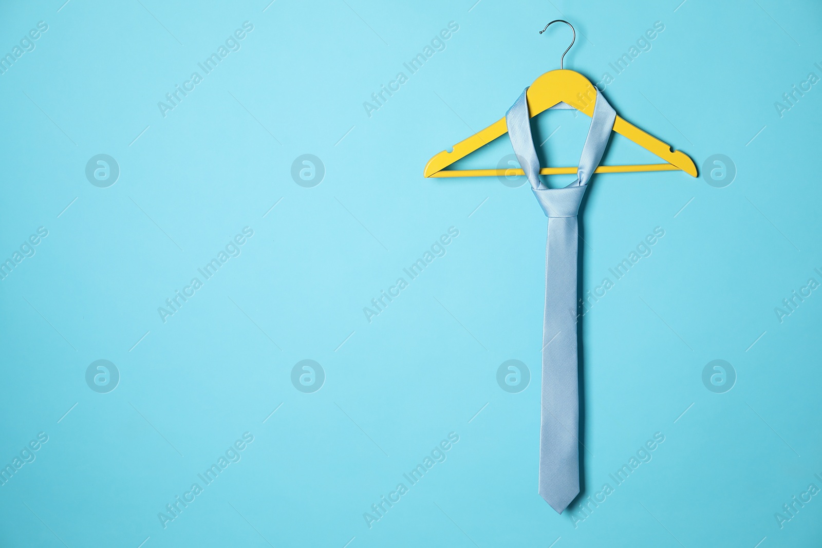 Photo of Hanger with silk tie on light blue background. Space for text