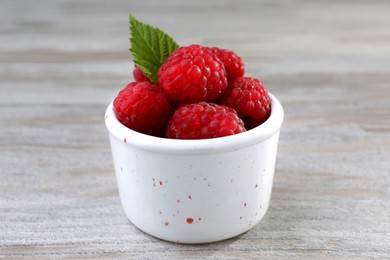 Photo of Tasty ripe raspberries and green leaf on white wooden table