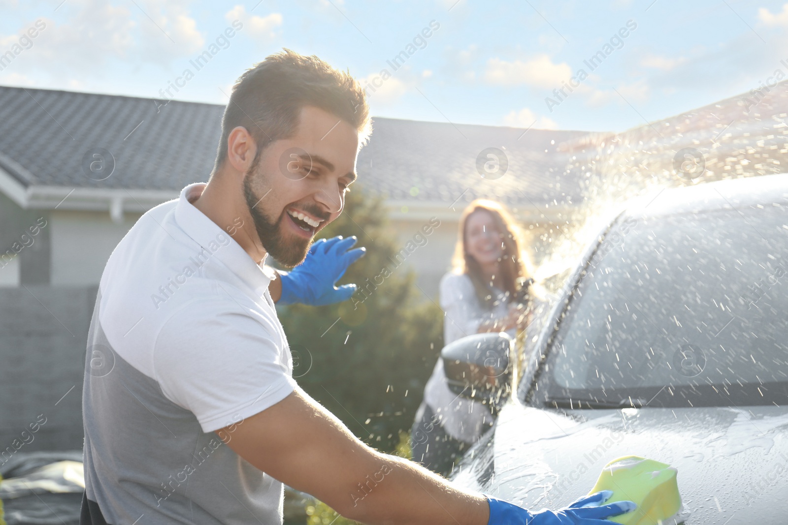 Photo of Happy couple washing car and having fun at backyard on sunny day