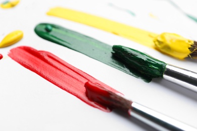 Photo of Brushes with different paints and strokes on white background, closeup