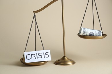 Photo of Scale with word Crisis and money on beige background
