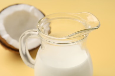 Glass jug of delicious vegan milk and coconut on yellow background, closeup