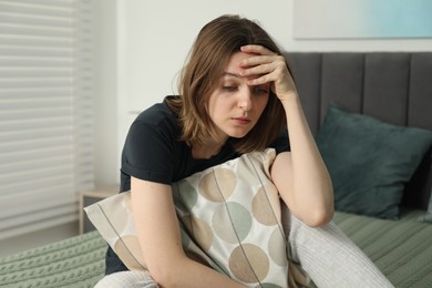 Photo of Sad young woman sitting on bed at home
