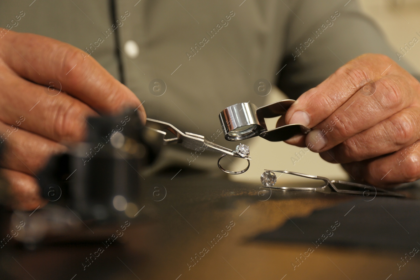 Photo of Professional jeweler working with beautiful ring at table, closeup