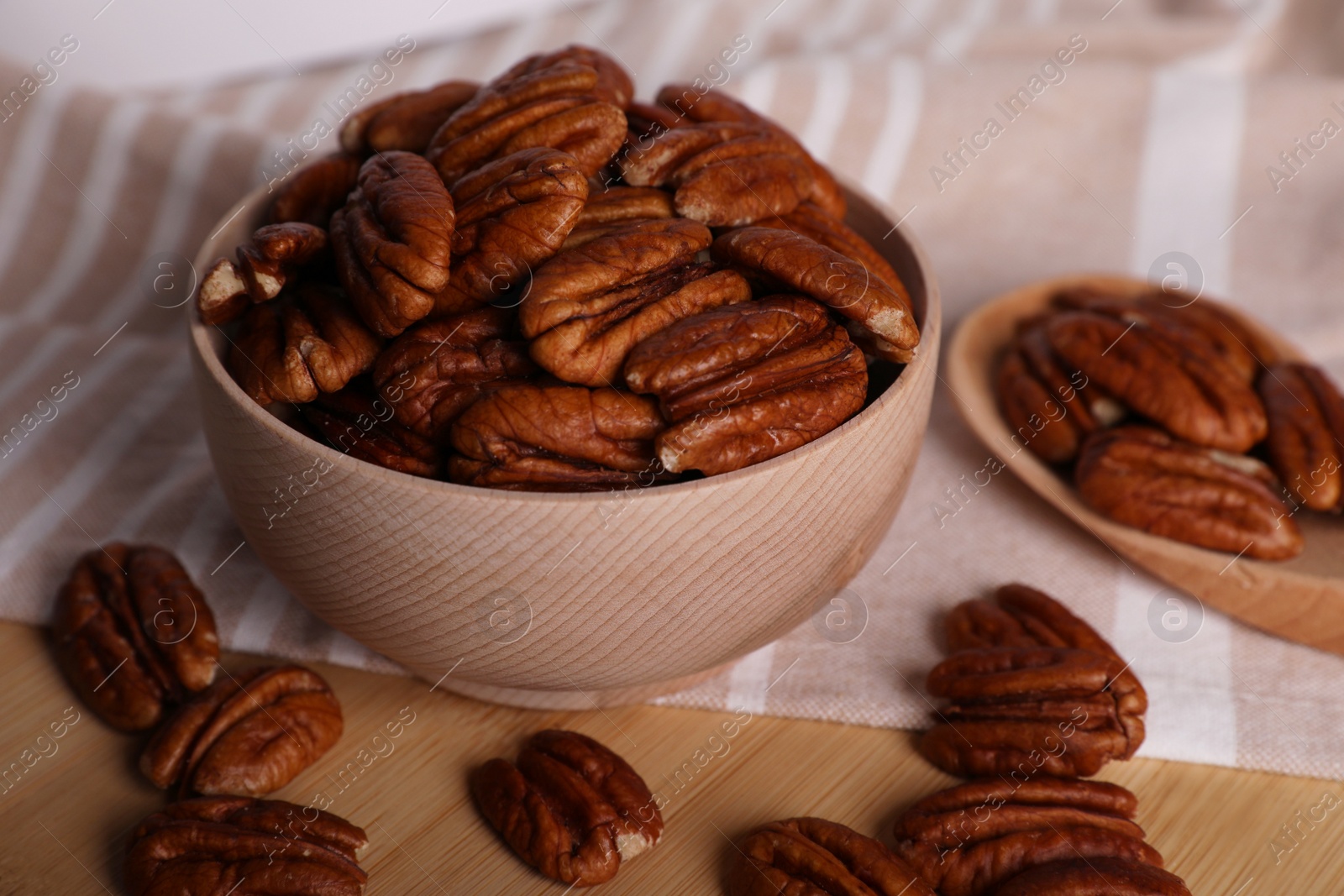 Photo of Tasty pecan nuts with bowl, spoon and cloth on wooden table, closeup