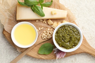 Photo of Tasty pesto sauce in bowl, basil, pine nuts, garlic, oil and cheese on light grey table, top view