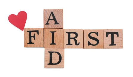 Words First Aid made of wooden cubes and cardboard heart isolated on white, top view