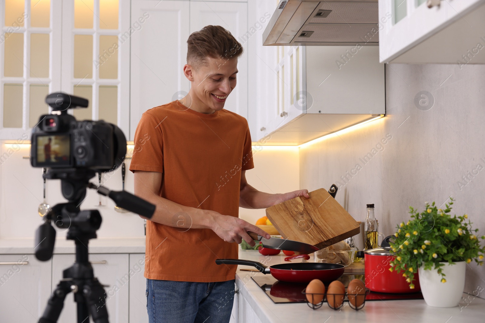 Photo of Smiling food blogger cooking while recording video in kitchen