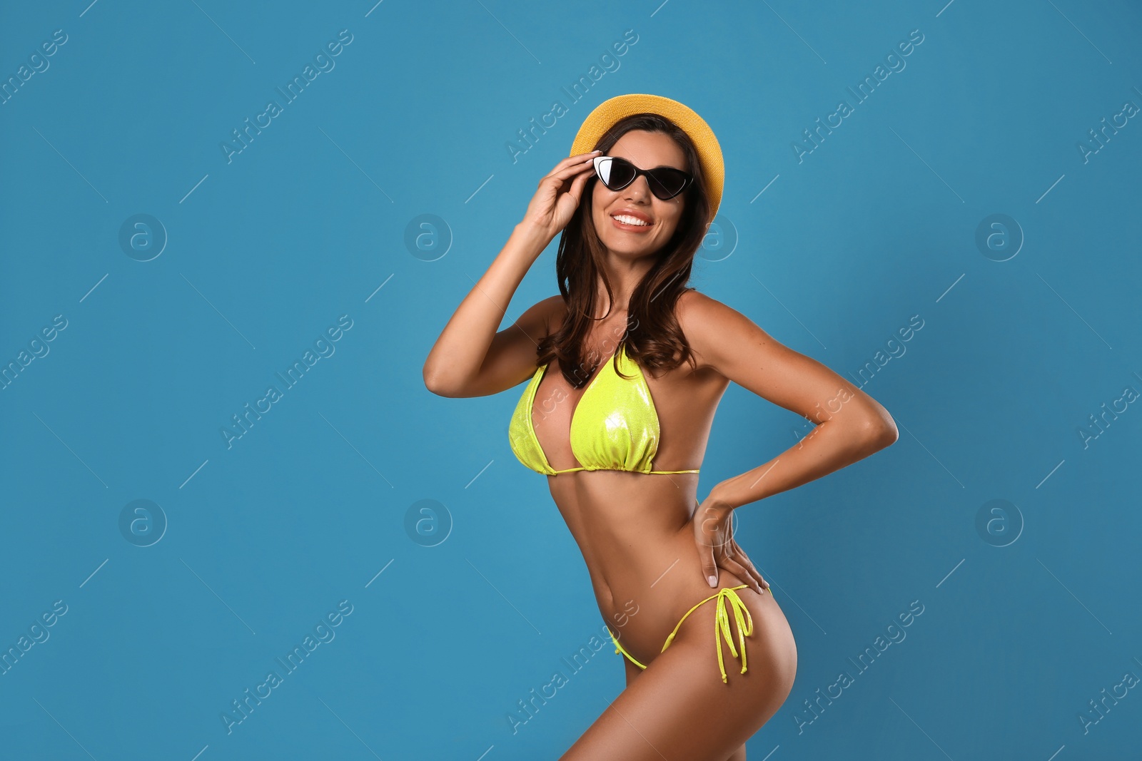 Photo of Beautiful woman in stylish bikini, sunglasses and hat on blue background. Space for text