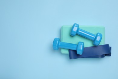 Photo of Two dumbbells, yoga block and fitness elastic band on light blue background, top view. Space for text