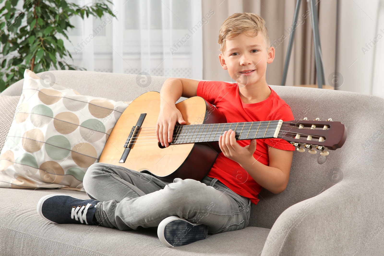 Photo of Cute little boy playing guitar on sofa in room