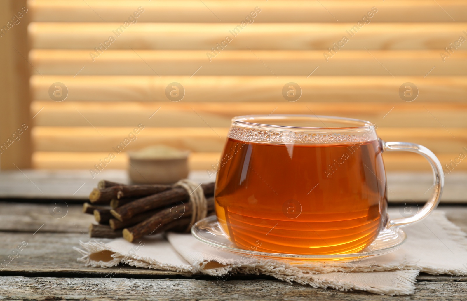 Photo of Aromatic licorice tea in cup and dried sticks of licorice root on wooden table. Space for text