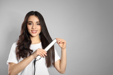 Photo of Happy woman using hair iron on grey background. Space for text