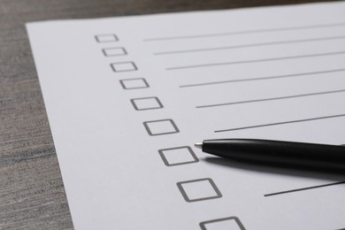 Photo of Paper sheet with checkboxes and pen on wooden table, closeup. Checklist