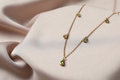 Photo of Elegant necklace on beige cloth, closeup. Stylish bijouterie
