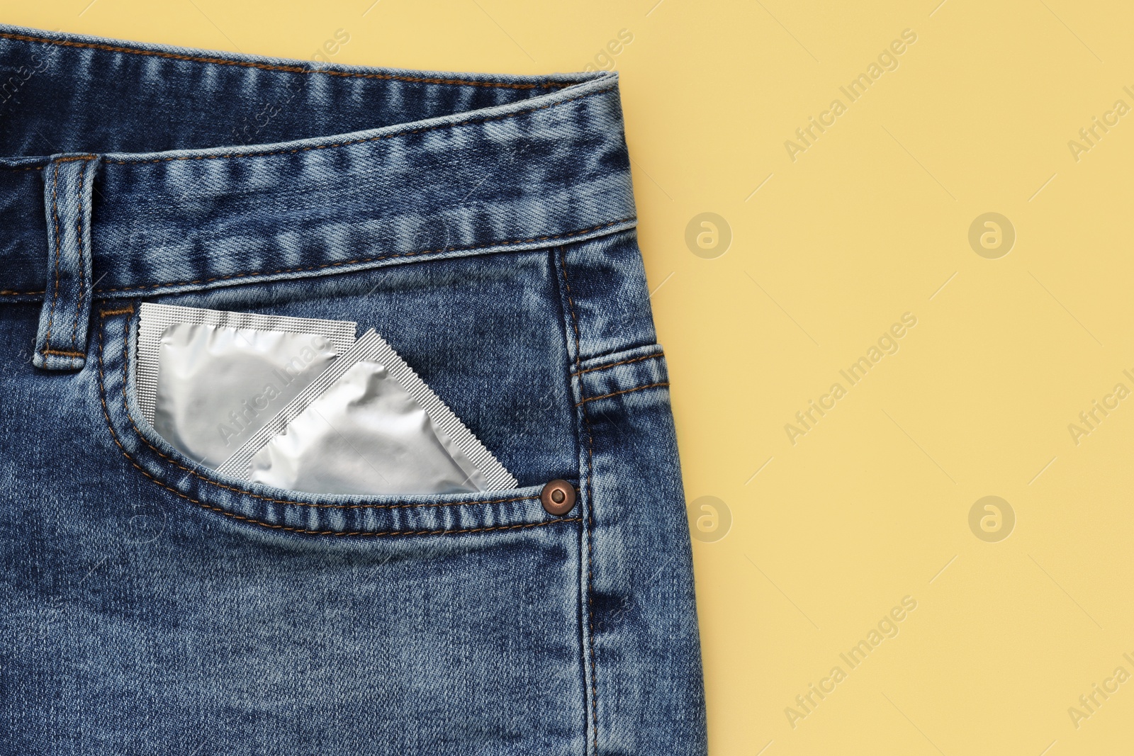 Photo of Packaged condoms in jeans pocket on beige background, top view. Safe sex