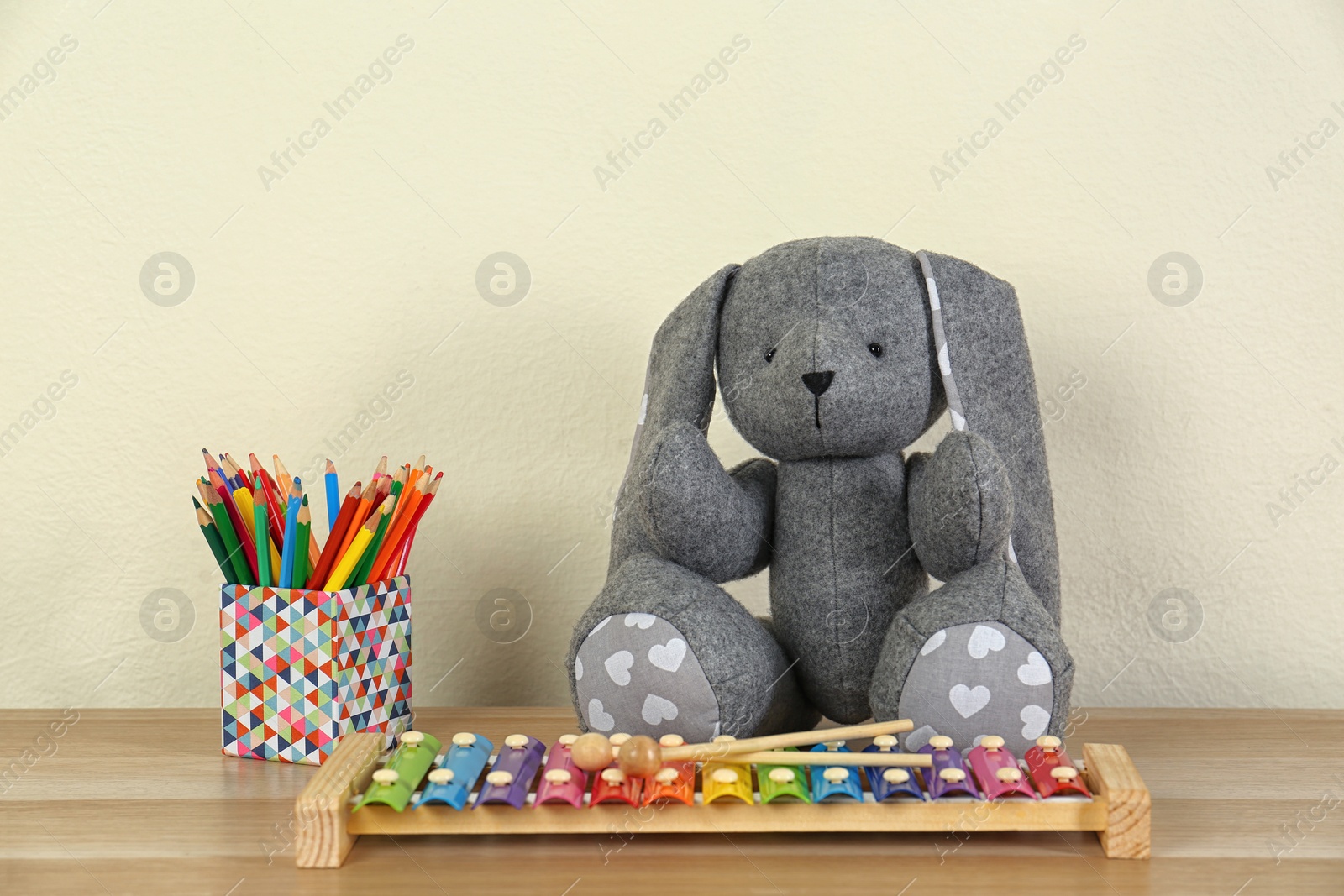 Photo of Toys and holder with color pencils for baby room interior on wooden table near light wall