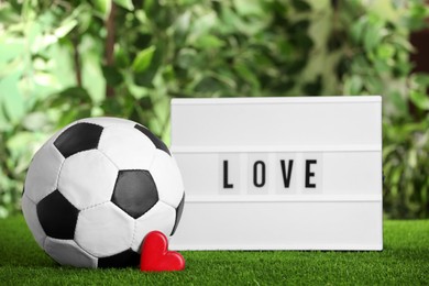 Photo of Football ball, lightbox with word Love and heart on green grass against blurred background