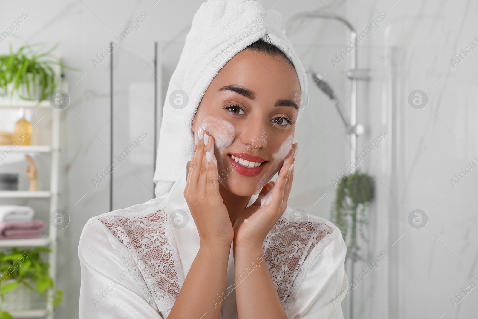 Photo of Beautiful young woman applying cleansing foam onto face in bathroom. Skin care cosmetic