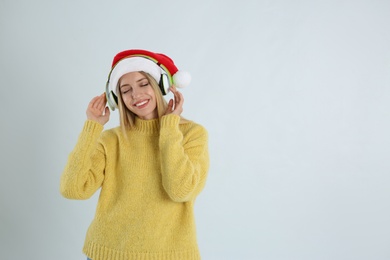 Photo of Happy woman with headphones on light grey background, space for text. Christmas music
