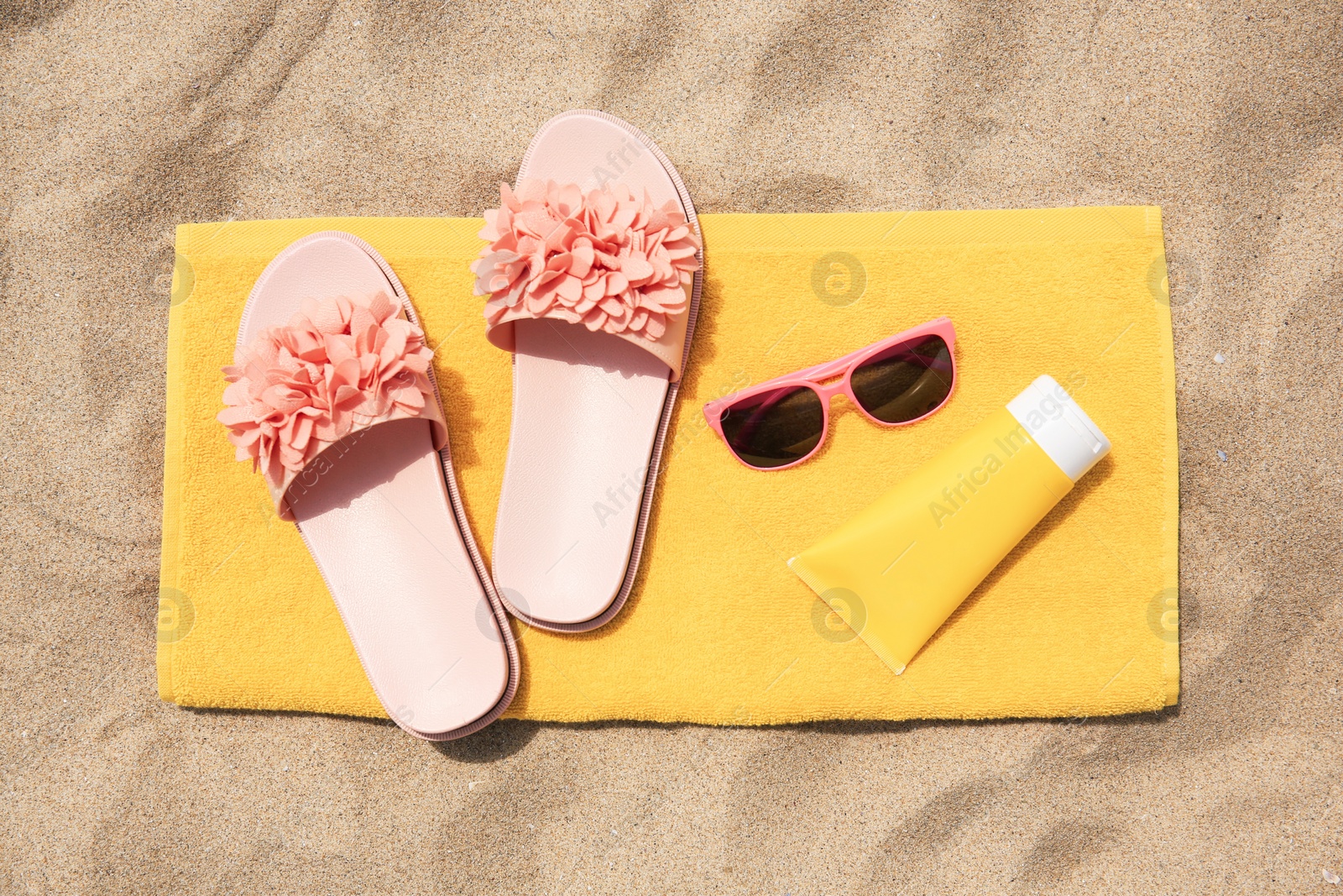 Photo of Slippers, towel, sunglasses and sunscreen on sand, flat lay. Beach accessories