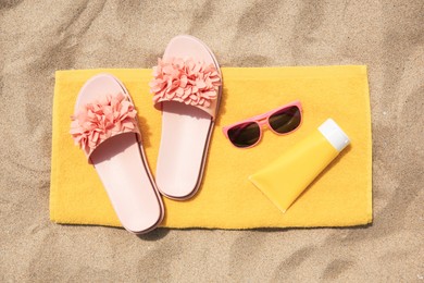 Photo of Slippers, towel, sunglasses and sunscreen on sand, flat lay. Beach accessories