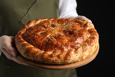 Photo of Woman holding tasty homemade pie on black background, closeup