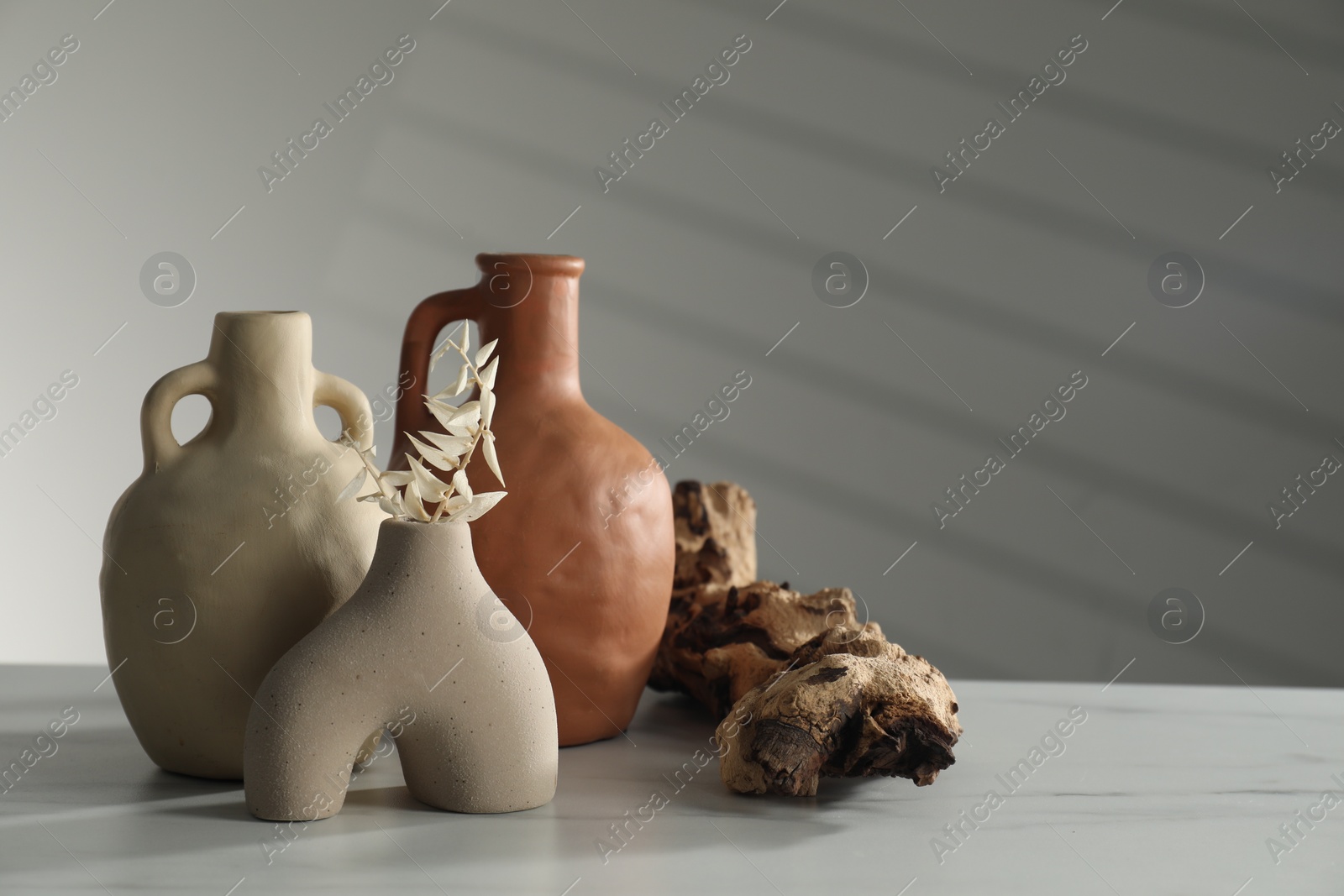 Photo of Clay flagons, vase, dried flowers and wooden snag on white marble table, space for text