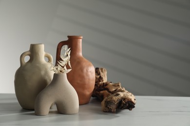 Clay flagons, vase, dried flowers and wooden snag on white marble table, space for text