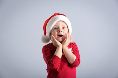 Photo of Cute emotional little boy wearing Santa Claus hat on light grey background