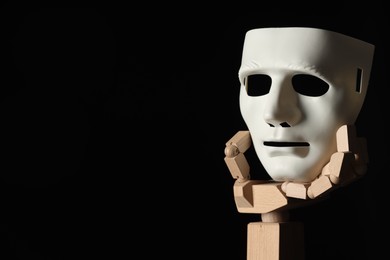 Wooden mannequin hand holding plastic mask on black background, space for text. Theatrical performance