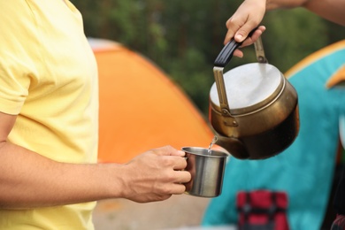Photo of Woman pouring drink into mug for man outdoors. Camping season