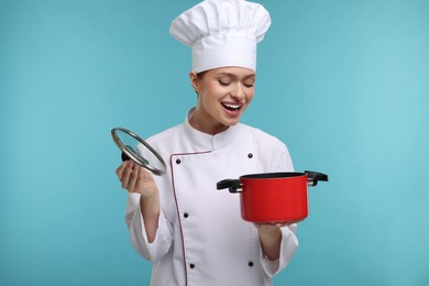 Photo of Surprised woman chef in uniform holding cooking pot on light blue background