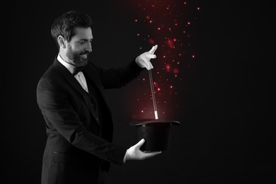Image of Smiling magician showing trick with wand and top hat. Black and white photo with red accent
