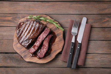 Photo of Delicious grilled beef meat and rosemary served on wooden table, flat lay