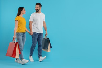 Photo of Happy couple with shopping bags on light blue background. Space for text