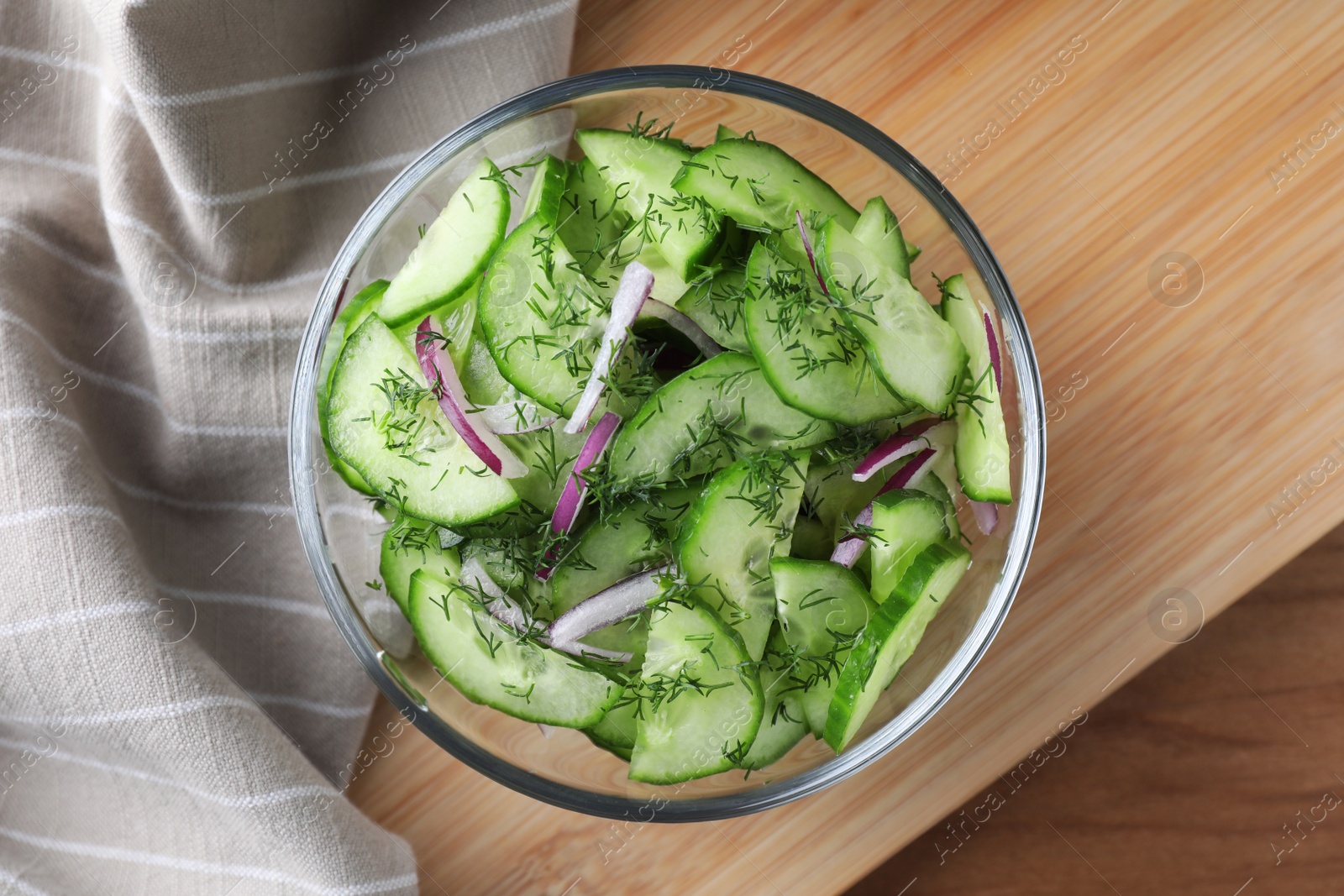 Photo of Bowl of tasty cucumber salad served on wooden table, flat lay