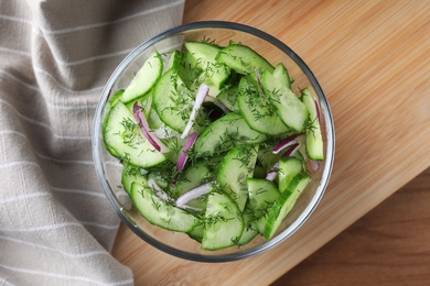 Photo of Bowl of tasty cucumber salad served on wooden table, flat lay