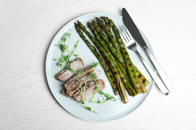 Photo of Tasty meat served with grilled asparagus on white wooden table, top view