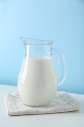 Photo of One jug of fresh milk on white table against light blue background