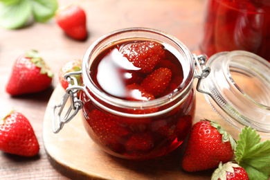 Photo of Delicious pickled strawberry jam and fresh berries on wooden table, closeup