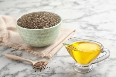 Sauce boat with chia oil, spoon and bowl of seeds on marble background