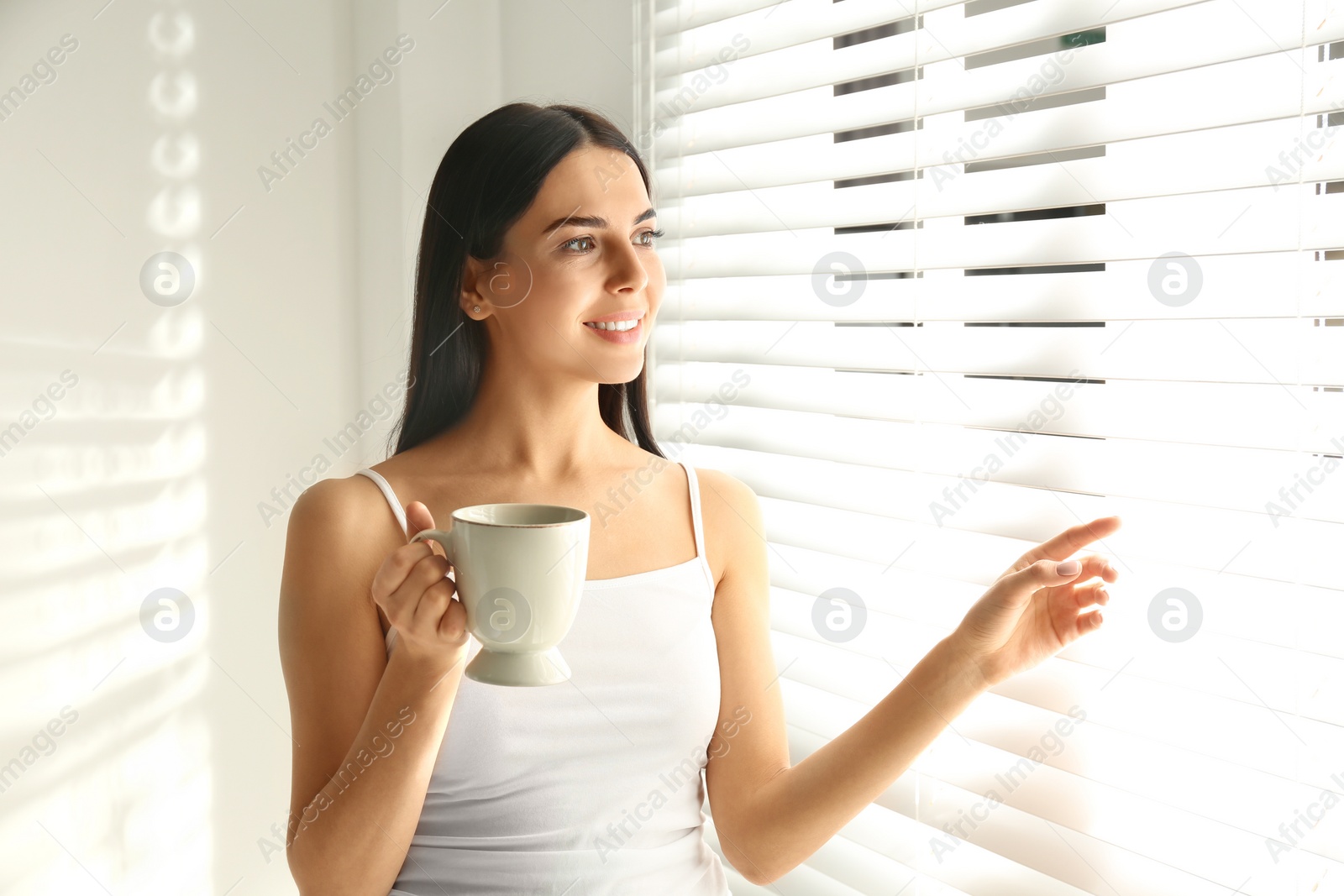 Photo of Young woman with cup of tea near window. Lazy morning