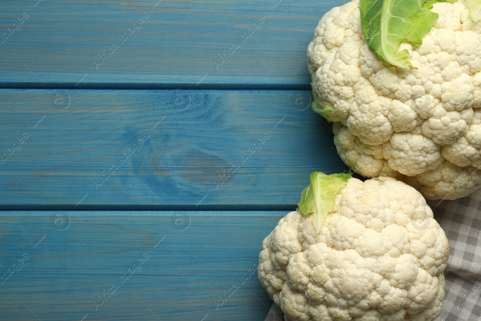 Photo of Fresh cauliflowers on light blue wooden table, top view. Space for text