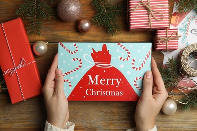 Photo of Woman holding Christmas card at wooden table, top view