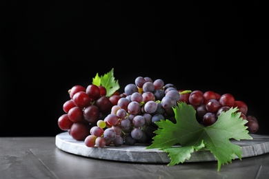 Photo of Fresh ripe juicy grapes on grey table against black background