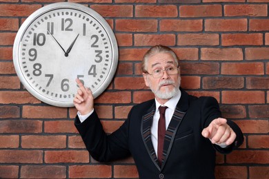 Photo of Angry senior boss pointing at clock on brick wall